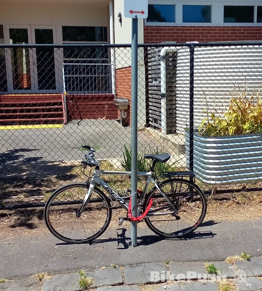 White bicycle locked to a street sign on the pavement beside the road