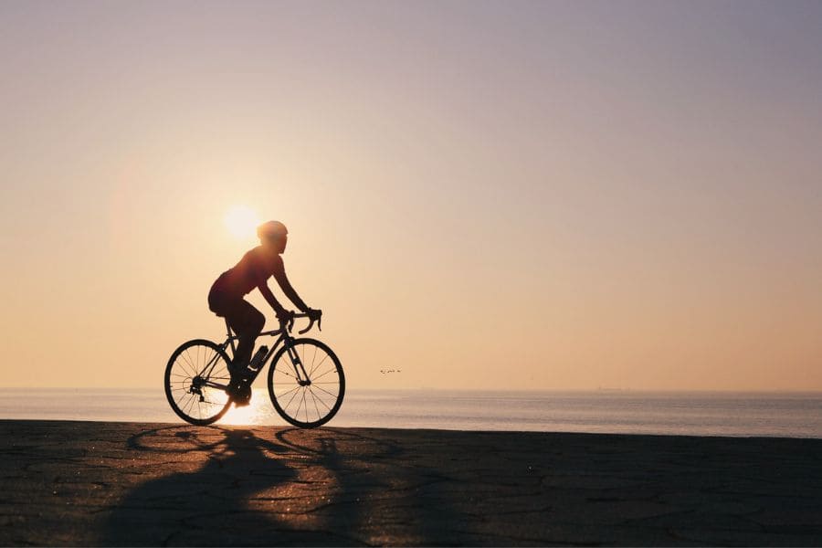 Cyclist on road bike with sun behind them beside the sea